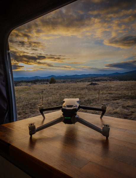 A drone on an RV's wooden table, framed by the window, overlooks a vibrant sunset landscape. Ideal for rv rental travel.