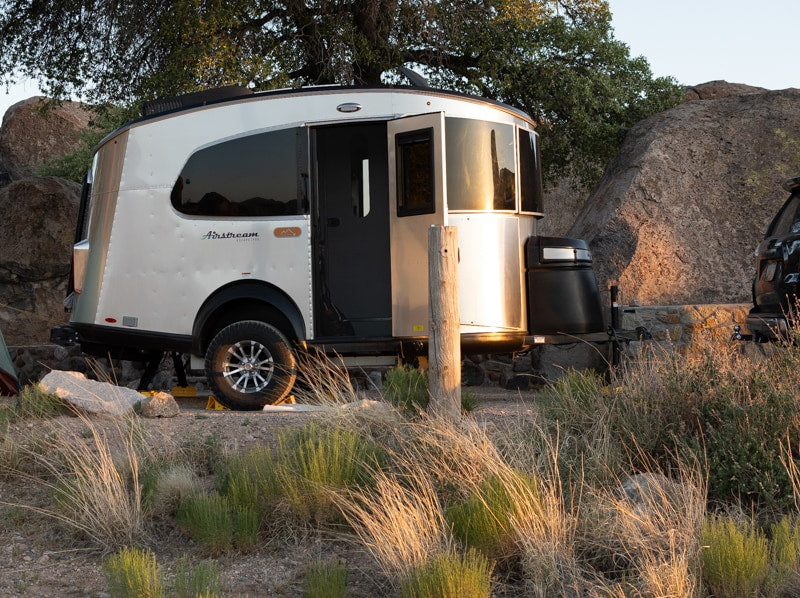 An Airstream Basecamp travel trailer, perfect for an rv rental outdoor adventure, set at a rocky campsite with warm sunset light.