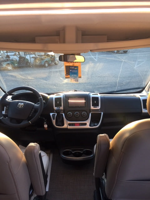 Driver's view inside an RV rental: dashboard, steering wheel, front seats, & outside view through windshield.