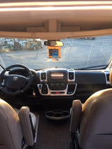 Driver's view inside an RV rental: dashboard, steering wheel, front seats, & outside view through windshield.