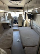 Modern rv rental interior showcasing kitchenette, lounge sofa, bed area, and driver's cab.