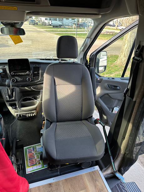 RV rental interior: Front of a camper van at a campground, showing seat, dash, and a pet leash attached. Ready for your adventure.