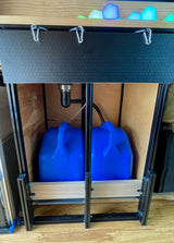 RV rental's under-sink water system: two blue jugs (fresh/grey water), connected to a drain within a custom cabinet.