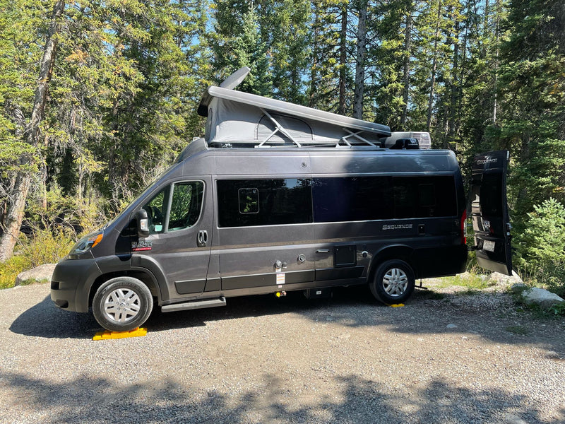 Gray pop-top camper van RV rental on gravel, leveled, surrounded by tall green trees. — photo 8