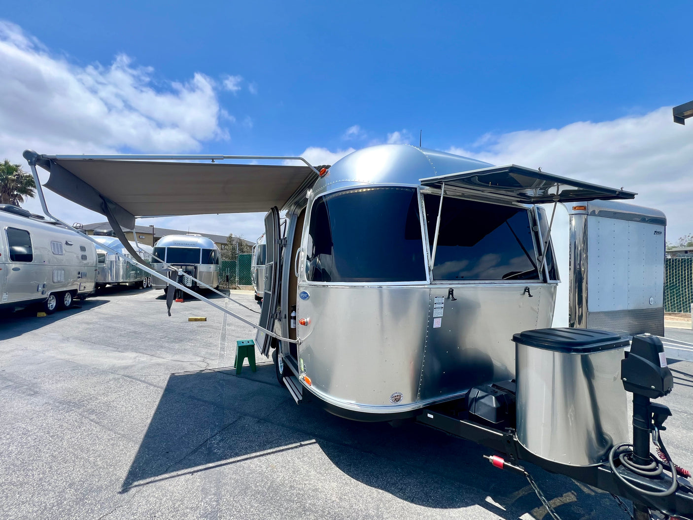 A shiny silver Airstream travel trailer for rv rental, with its awning extended, parked in an outdoor lot.
