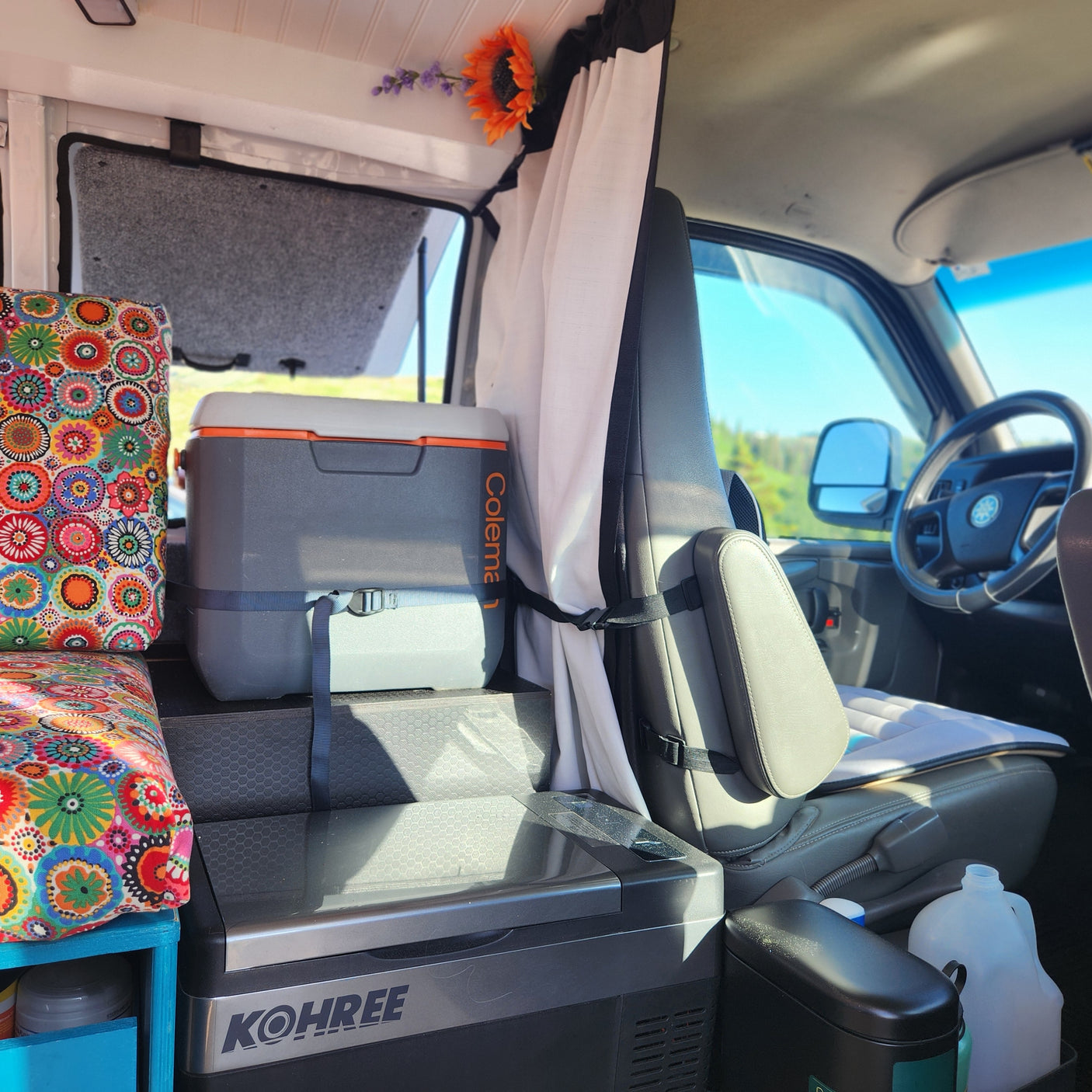 RV rental interior with vibrant cushions, Coleman cooler, and Kohree fridge setup for van life adventures.