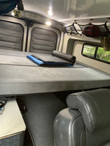 Inside an RV rental: a comfortable bed with a sleeping pad, overhead storage, and a view outside.