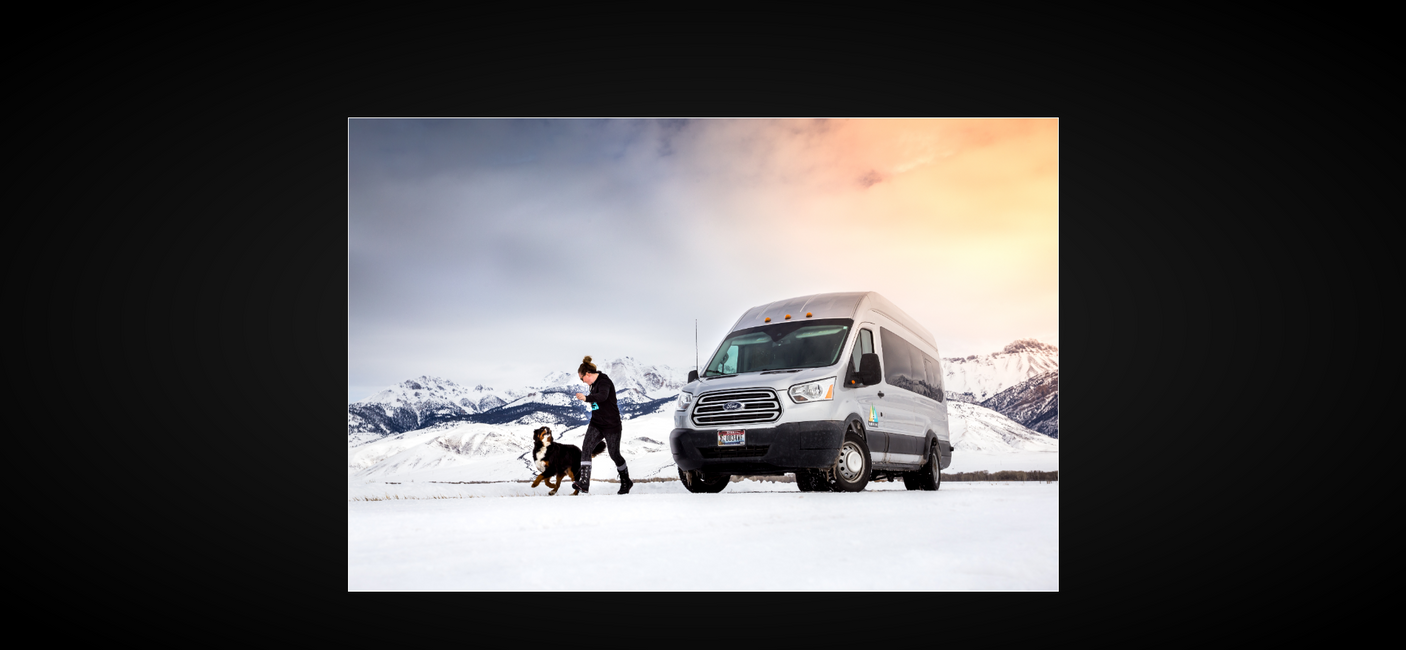 Enjoy winter with an RV rental! A woman and her dog explore snowy mountains beside a silver van, perfect for pet-friendly adventures.