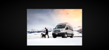 Enjoy winter with an RV rental! A woman and her dog explore snowy mountains beside a silver van, perfect for pet-friendly adventures.