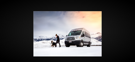 Enjoy winter with an RV rental! A woman and her dog explore snowy mountains beside a silver van, perfect for pet-friendly adventures.