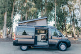 Gray Ram ProMaster camper van rv rental with pop-top up, side door open, revealing compact kitchen. Ideal for adventure.