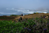 Coastal tranquility: a couple enjoys foggy ocean views from a cliffside with wildflowers. Ideal RV rental destination.
