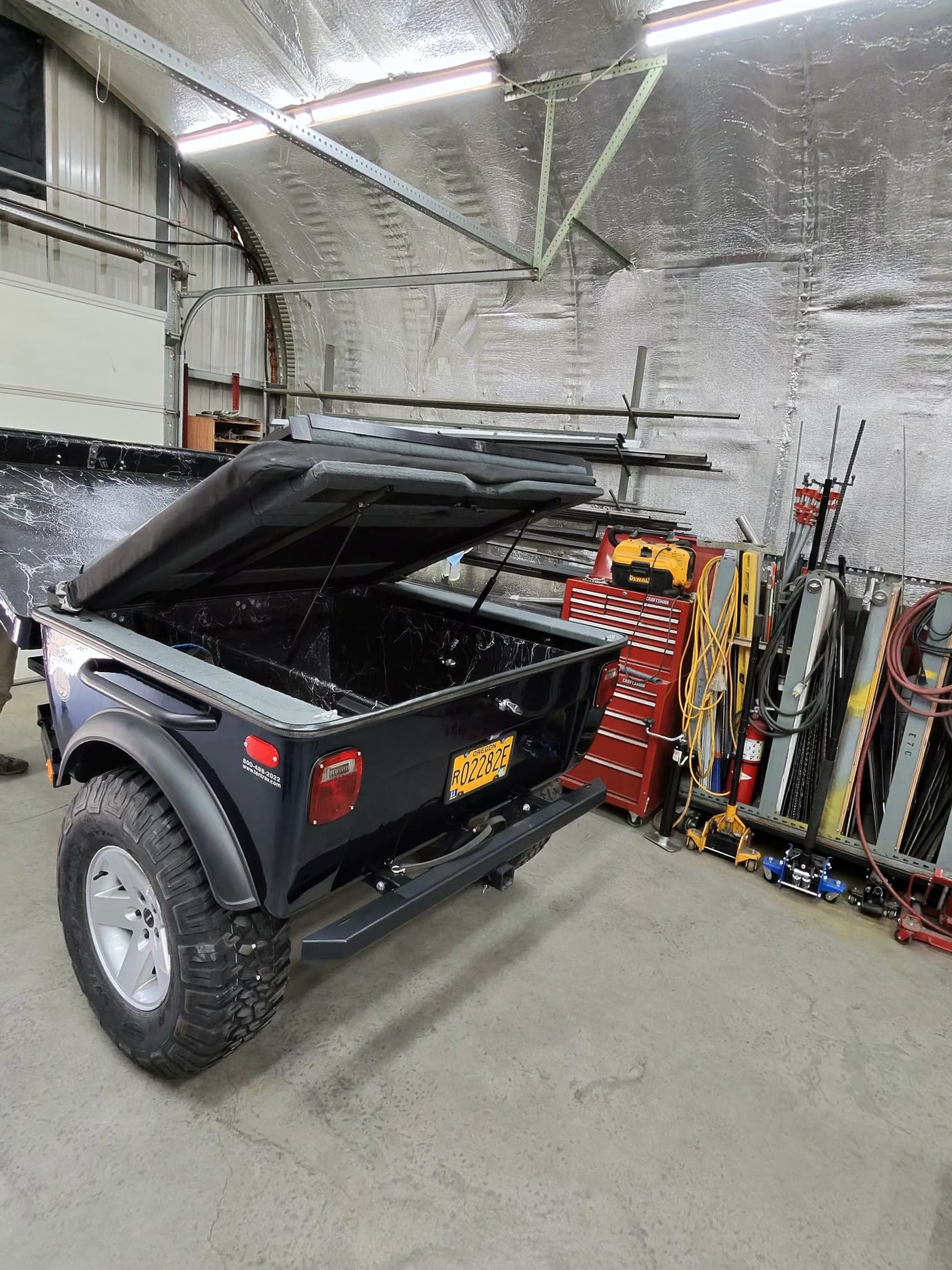 Rugged utility trailer with open bed and off-road tires, perfect for your next rv rental camping trip, inside a workshop. — photo 6