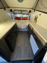 Cozy rv rental interior with bed, dual countertops, a mini-fridge, and climate control, offering a comfortable travel space.