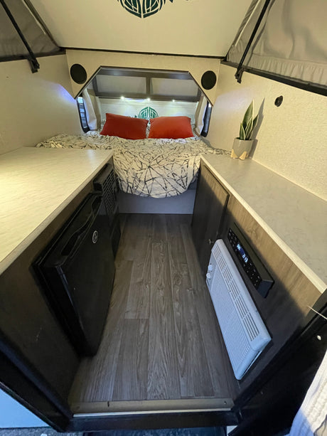 Cozy rv rental interior with bed, dual countertops, a mini-fridge, and climate control, offering a comfortable travel space.