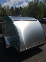 A stylish silver and teal teardrop trailer parked outdoors, reflecting sunlight. Consider this compact rv rental for your next trip.