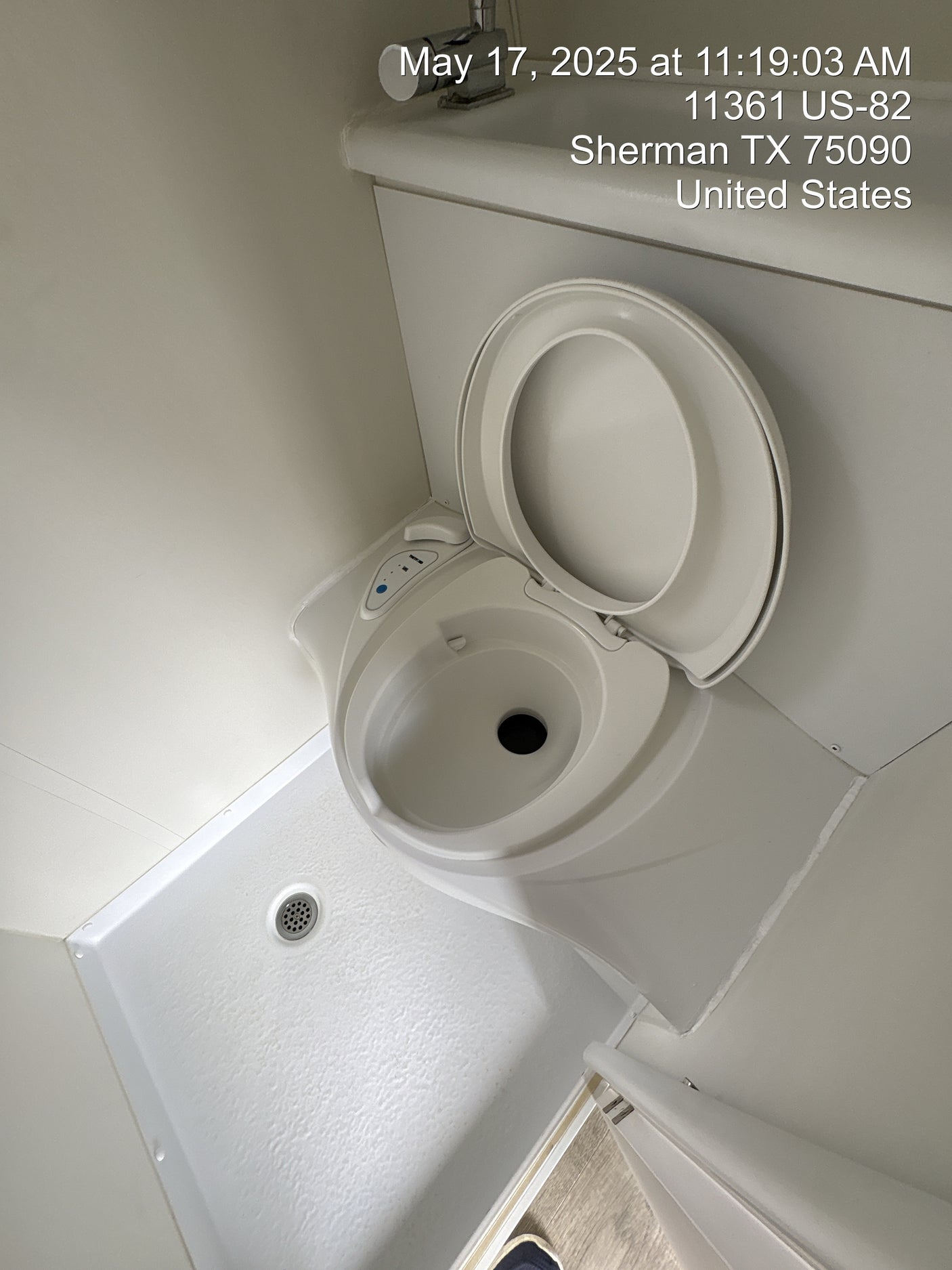 Inside an RV rental, showing a compact white toilet with open lid and an adjacent shower pan with drain.