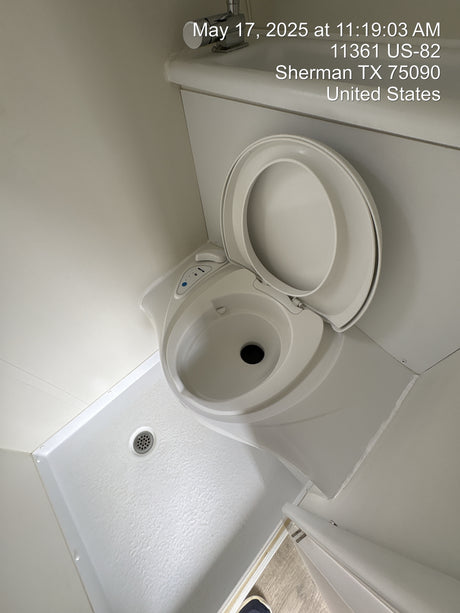 Inside an RV rental, showing a compact white toilet with open lid and an adjacent shower pan with drain.