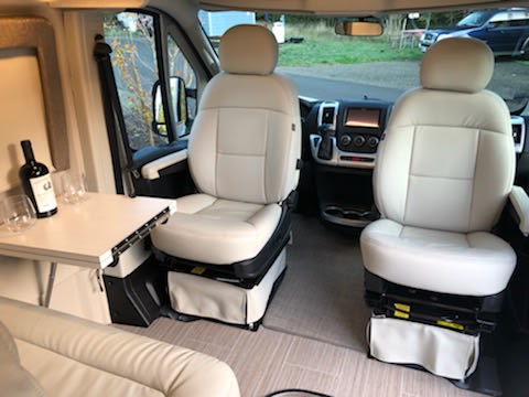 Experience our cozy rv rental interior: Swiveled cabin seats, wine bottle, and glasses on a side table. Ready for comfort! — photo 11