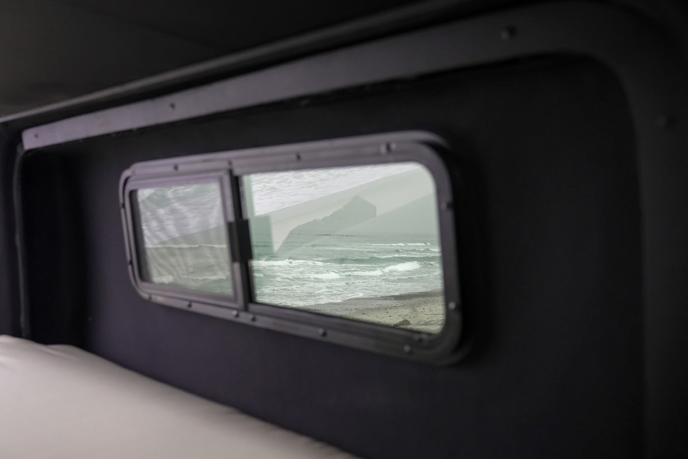 Cozy RV rental interior, window offers ocean beach view with waves & distant bluff. Ideal for travel. — photo 9