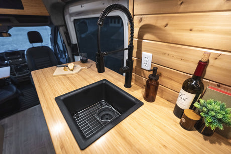 RV rental: Stylish camper van kitchen with bamboo counters, black sink, wine, and fresh pear, offering home comforts.
