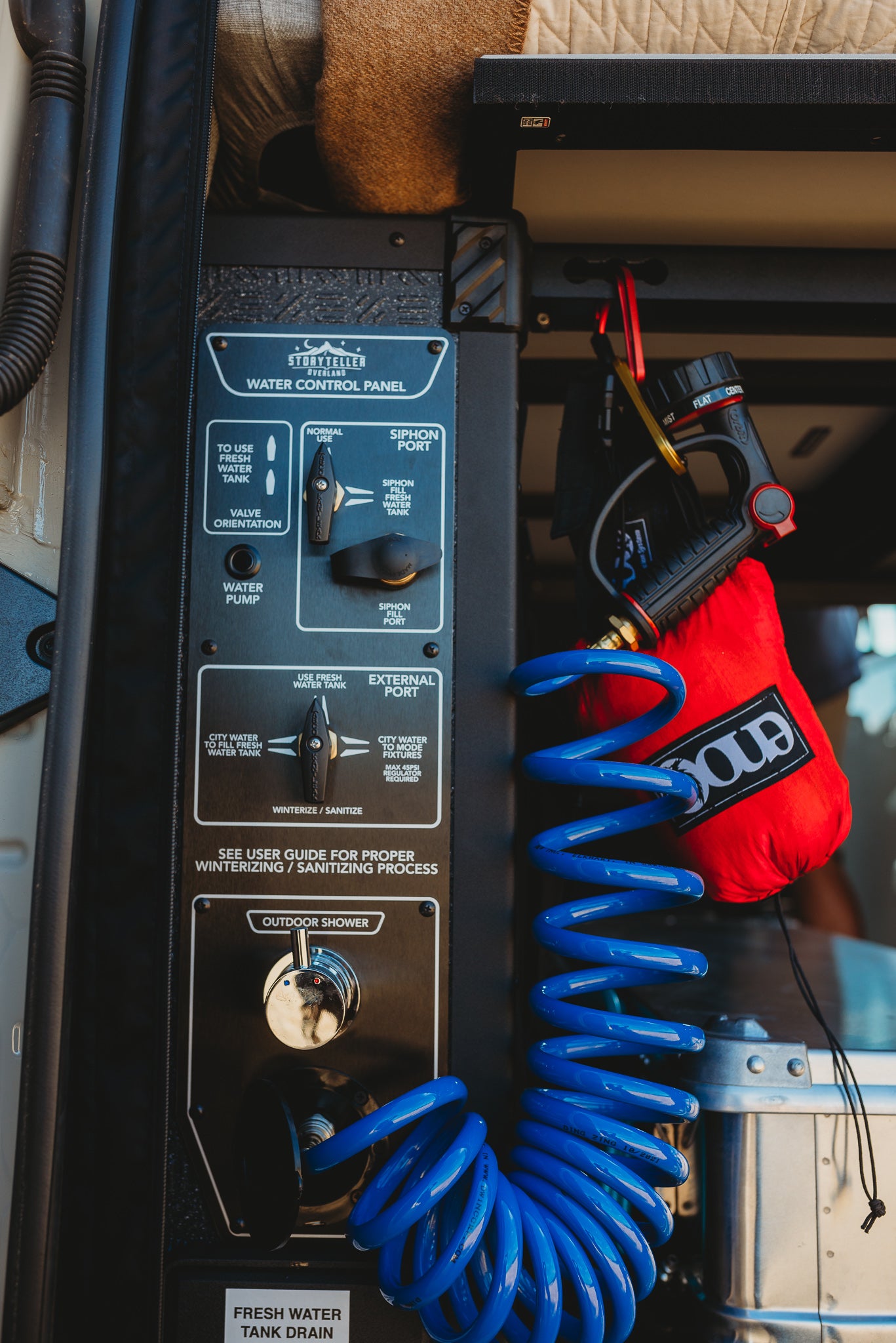 RV rental's water system: control panel, outdoor shower, and blue coiled hose. Perfect for off-grid camping.