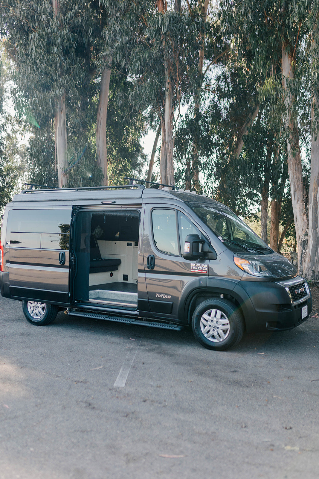 Gray Ram ProMaster camper van RV rental parked with side door open, showing interior conversion. Perfect for a road trip.