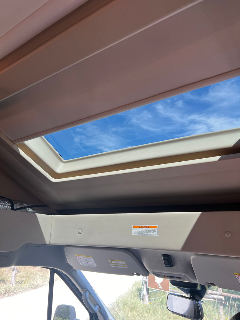 RV rental interior view: Bright skylight with blue sky, above a cozy over-cab bunk and driver's cabin. — photo 13