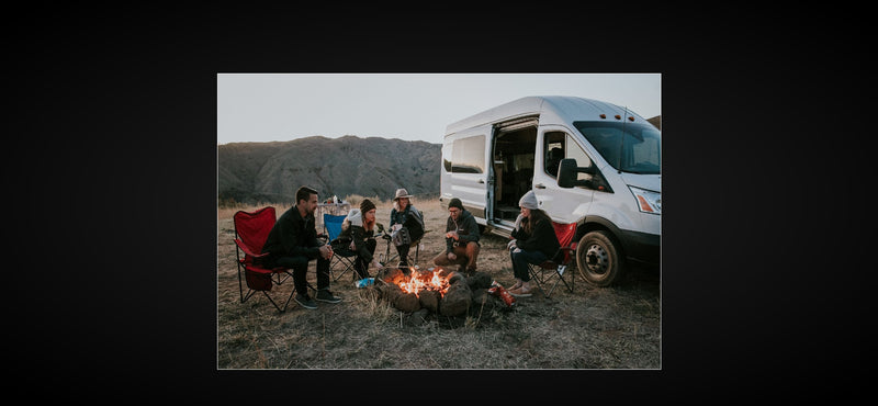 Gathered around a campfire, friends relax near their white RV rental amidst a natural landscape. — photo 14