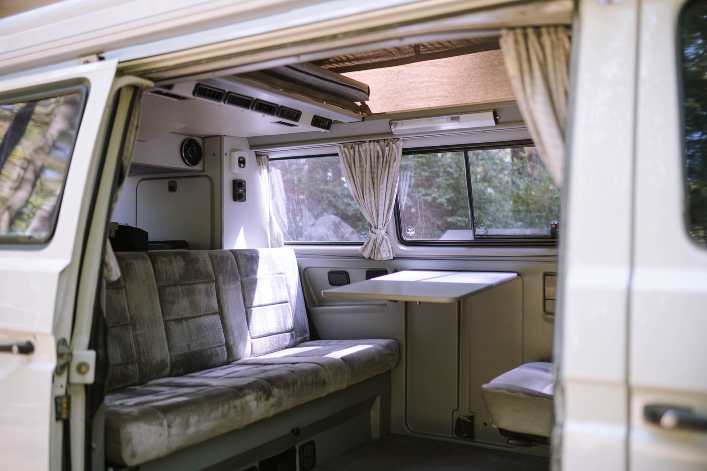 Interior of an RV rental camper van, showing a comfortable bench seat, fold-down table, and windows with curtains, perfect for travel.