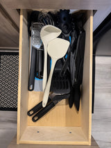 RV rental kitchen drawer filled with essential cooking utensils: whisks, spatulas, knives, and a grater.