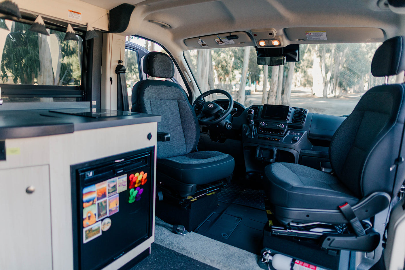 RV rental interior with a compact kitchen, fridge (magnets), and front cabin seats for a cozy, road trip-ready setup.