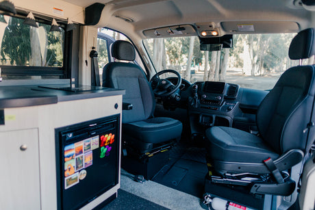 RV rental interior with a compact kitchen, fridge (magnets), and front cabin seats for a cozy, road trip-ready setup.