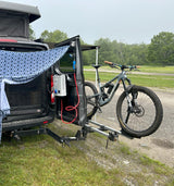 This RV rental camper van features a pop-top, outdoor shower, and a mountain bike on its rear rack, parked in a grassy area.