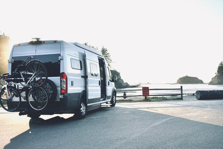 RV rental with bikes on back, parked by a sunny beach with ocean views. Perfect for coastal travel and adventure.