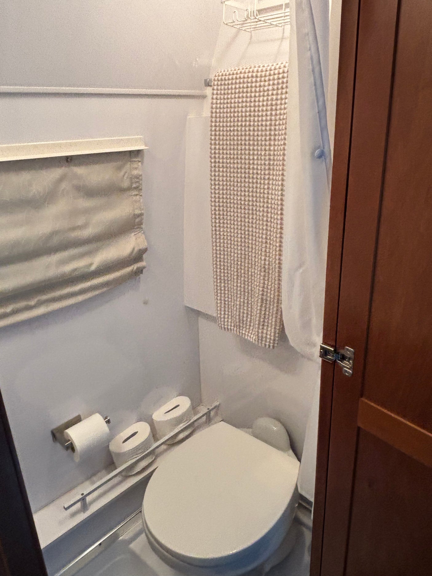 Compact RV rental bathroom: toilet, shower curtain, hanging towel, and toilet paper storage. Efficient space for travel.