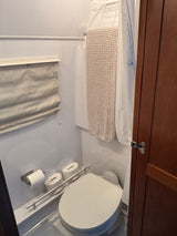 Compact RV rental bathroom: toilet, shower curtain, hanging towel, and toilet paper storage. Efficient space for travel.