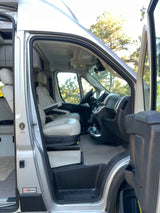 Spacious rv rental camper van interior from side door, showing modern cab, swivel seats, and part of living area.