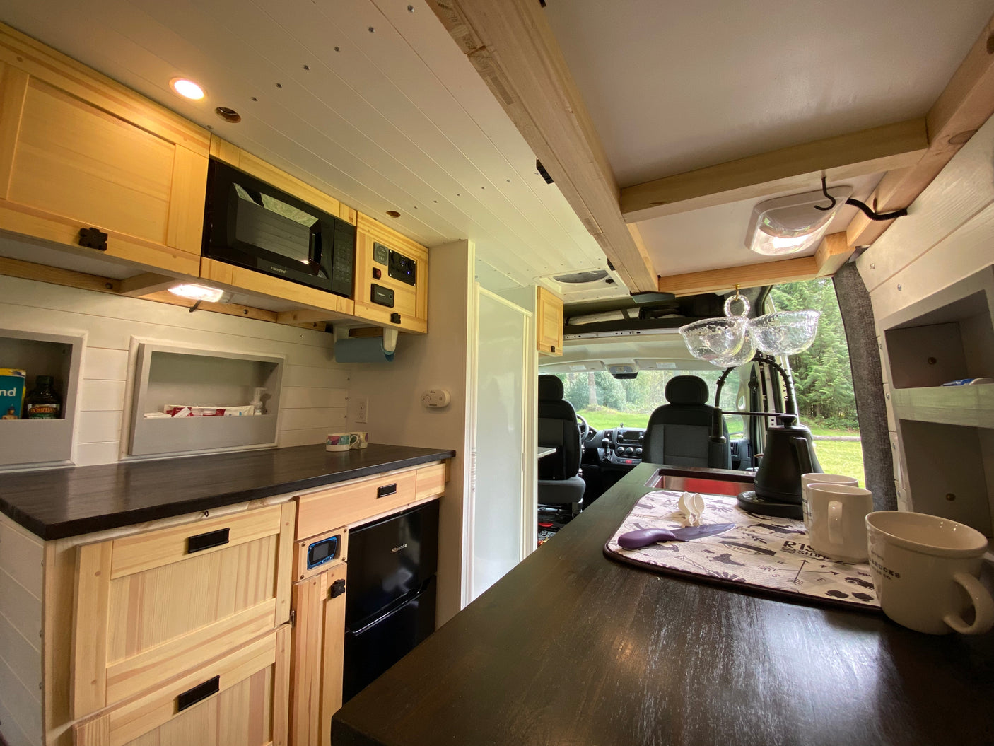 RV rental's custom kitchen boasts wooden cabinets, microwave, fridge, and dark counters. Ideal for adventures.