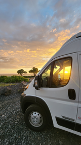 Golden sunset bathes an RV rental parked by the ocean. Ideal for a serene travel adventure on a rocky coast.