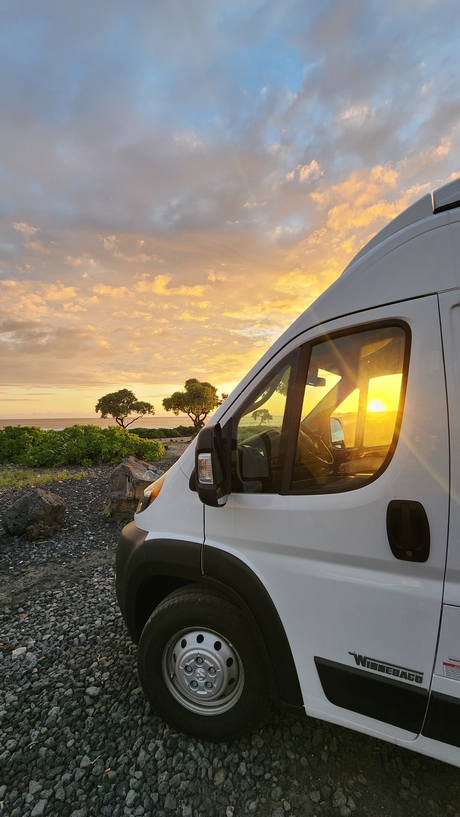 Golden sunset bathes an RV rental parked by the ocean. Ideal for a serene travel adventure on a rocky coast.
