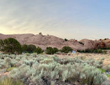 Scenic desert campsite with a white RV rental, surrounded by light-colored rock formations & sagebrush. Perfect for outdoor adventures.