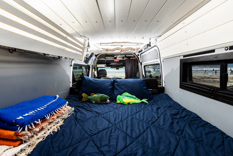 This cozy rv rental interior features a comfy bed with fish toys, stacked blankets, and open doors revealing a beach view.