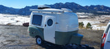 RV rental: A cozy Happier Camper travel trailer parked overlooking a beautiful snowy mountain landscape, perfect for adventure.