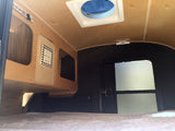 Cozy RV rental interior: bed, wooden storage, and overhead fan for comfortable mobile living.