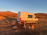 Autumn RV rental camping scene: white van, person, dog, and mountains at sunset. Perfect outdoor escape.