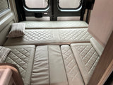 RV rental interior: Comfortable, quilted bed & seating area in a camper van, with rear windows and an "EXIT" sign.