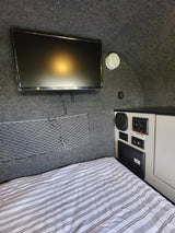 RV rental interior: TV, bed, smoke detector, and amenities control panel on gray carpet with mesh mat.