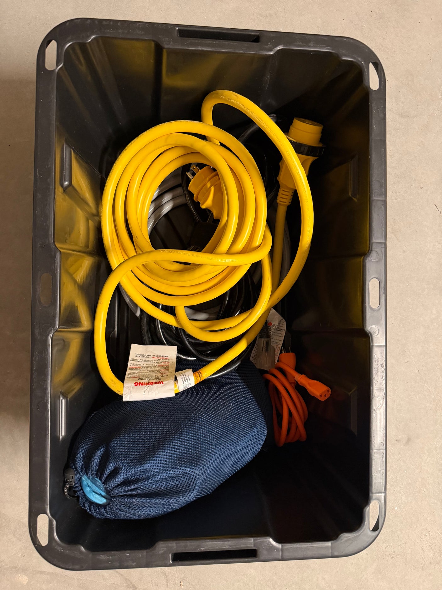 Black bin with RV rental shore power cables (yellow, orange) and a blue bag, essential electrical hookup gear.