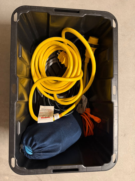 Black bin with RV rental shore power cables (yellow, orange) and a blue bag, essential electrical hookup gear.